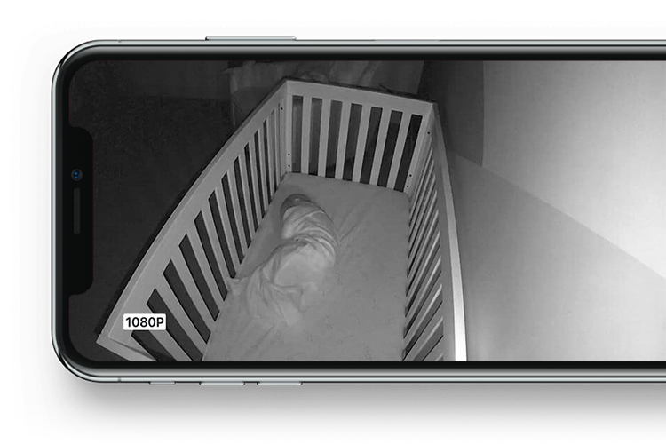 暗い部屋のベッドの中で寝ている赤ちゃんを映しているiPhoneの画面。