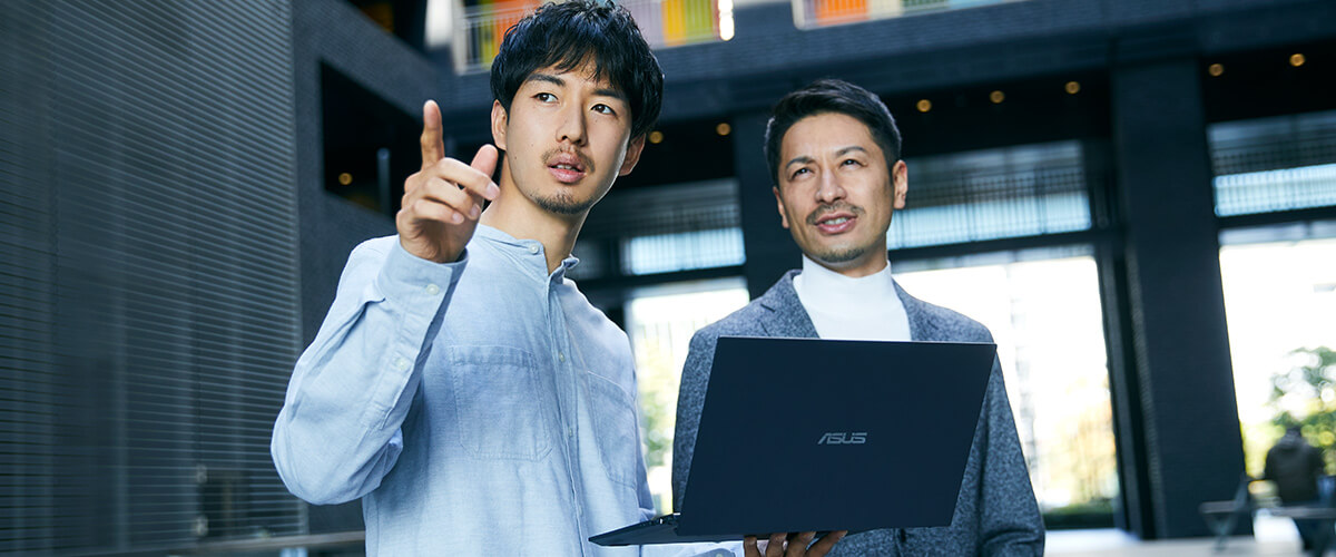 画面を開いているASUS ExpertBook B9を片手で持ちながら、人と話している写真