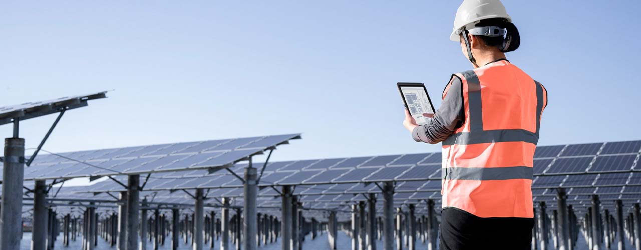 屋外の太陽光発電施設で、安全ヘルメットとベストを着用した作業員がLenovo ThinkTab X11タブレットを操作している様子。